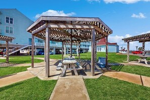 Ein Pavillon mit einem Picknicktisch in der Mitte, umgeben von einer Rasenfläche unter blauem Himmel.