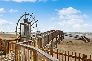 A wooden boardwalk leading to a beach with a large wheel structure. - Seascape Condos - Day Break at the Seascape #2219 (Galveston)