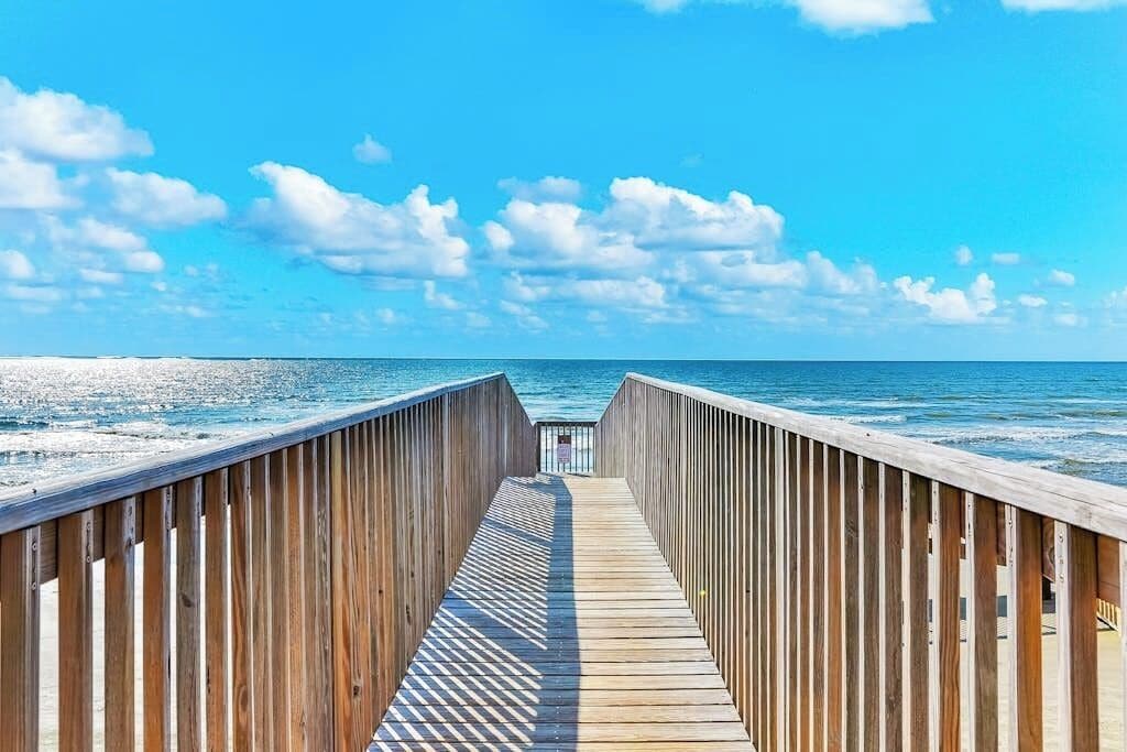 A wooden boardwalk leading to the beach with a clear sky above.