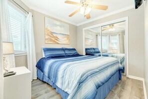 Ein Schlafzimmer mit einem Bett, einem Deckenventilator, einem Gemälde und einem Spiegel.