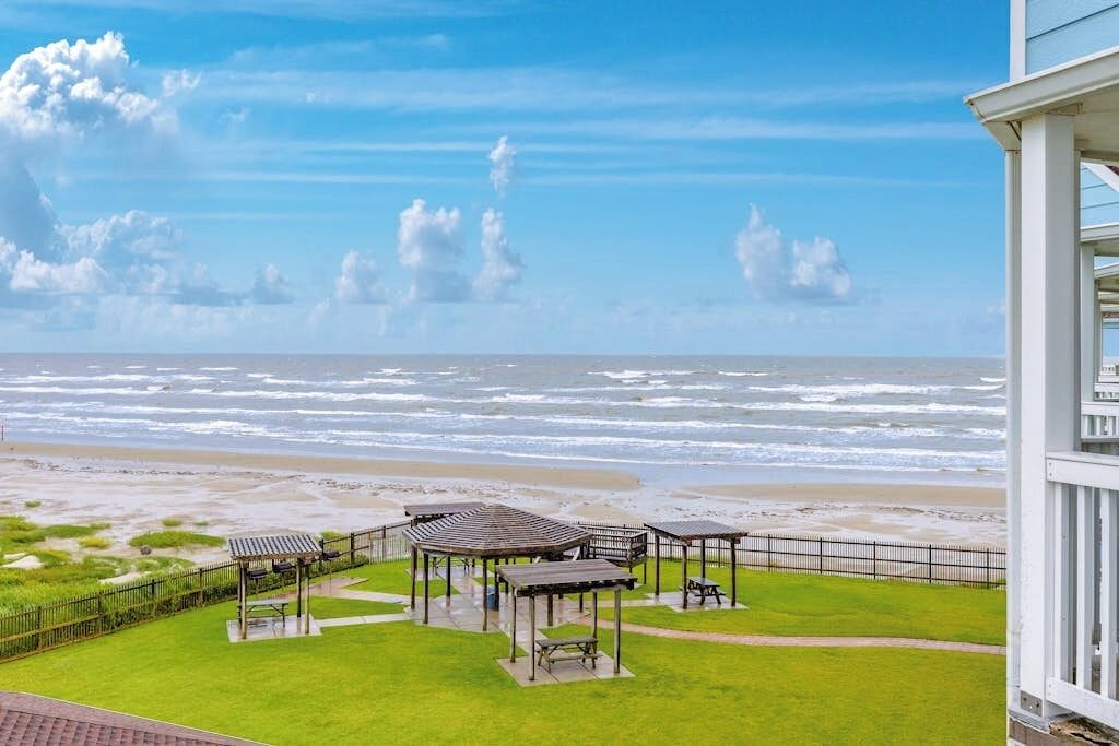 Eine Küstenansicht mit einer Wiese, einem Strand und einem Gebäude mit einem Balkon.