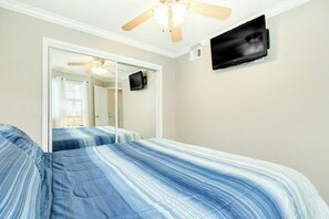 A bedroom with two beds, a ceiling fan, a flat-screen TV, and a mirror. - Seascape #2319 Beach Happy (Galveston)