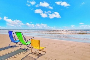 Two beach chairs on a sandy beach with a clear sky and ocean in the background. - Seascape #2319 Beach Happy (Galveston)