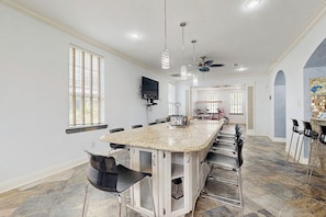 A spacious kitchen with a large island, bar stools, and a ceiling fan. - Sandcastle Retreat - Heart of Galveston, Dogs OK (Galveston)