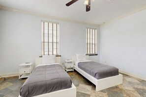 A bedroom with two beds, white nightstands, and a ceiling fan. - Sandcastle Retreat - Heart of Galveston, Dogs OK (Galveston)