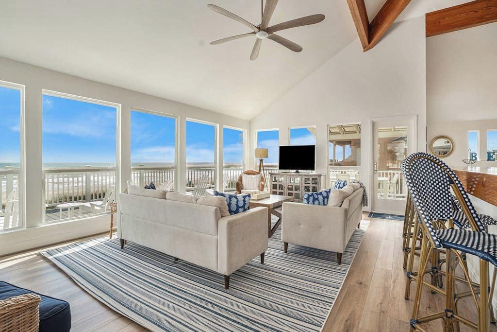 A spacious living room with a large window, a ceiling fan, and a view of the ocean.