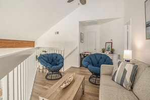 Un salon moderne avec un plancher en bois, un canapé, deux fauteuils bleus, une table basse et un escalier menant à un autre niveau.