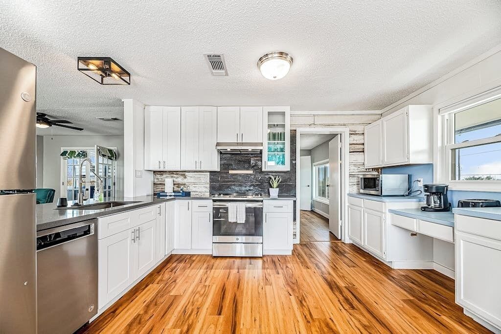 A modern kitchen with white cabinets, a stainless steel refrigerator, and a wooden floor.