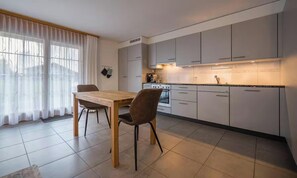 Une cuisine moderne avec des meubles blancs, une table à manger en bois et une chaise noire.