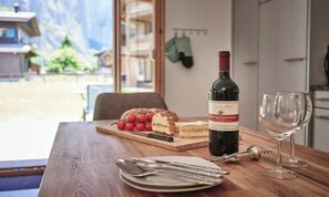 A dining table with a bottle of wine, a glass, and a cheese board with fruits and cheese. - ELEGANT CHALET APARTMENT IN THE HEART OF LAUTERBRUNNEN (Lauterbrunnen)