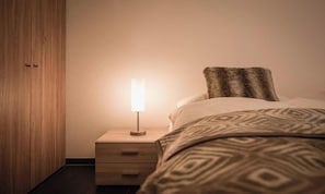 A bedroom with a bed, a bedside table with a lamp, and a wooden wardrobe. - ELEGANT CHALET APARTMENT IN THE HEART OF LAUTERBRUNNEN (Lauterbrunnen)
