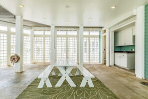 A spacious room with a large table and benches, a kitchen area, and large windows with a view. - Ship Shape - Gulf Views, Walk to the Beach, Pet's Welcome! (Galveston)