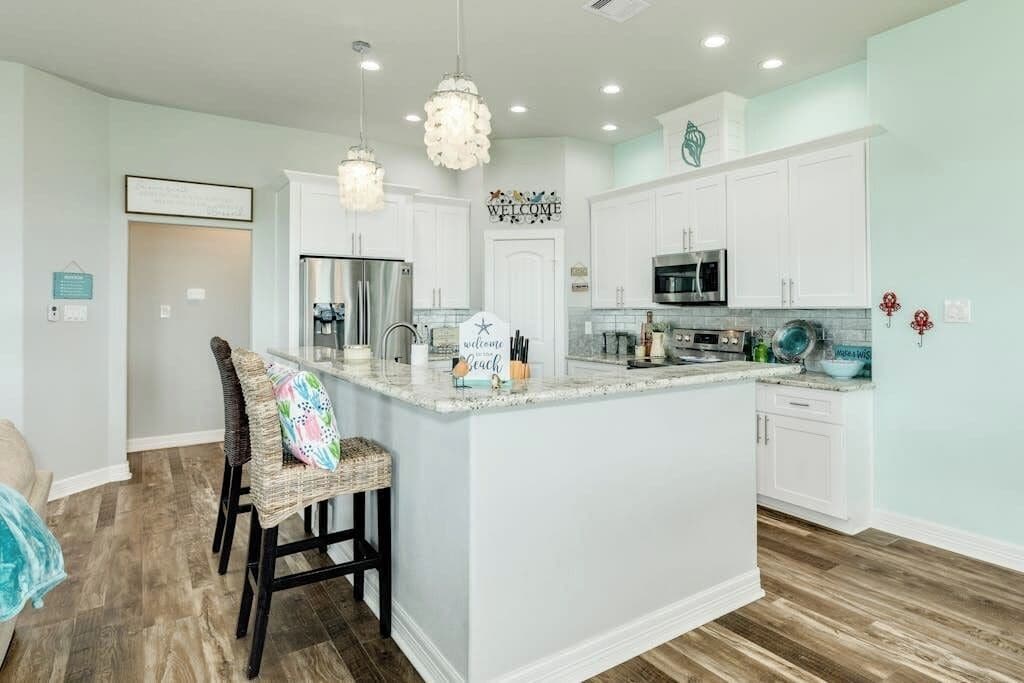 A modern kitchen with white cabinets, a central island, and a stainless steel refrigerator.