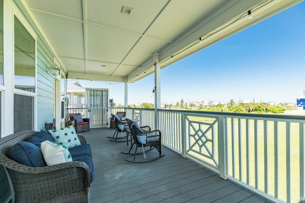 A covered porch with wicker furniture and a view of the ocean.