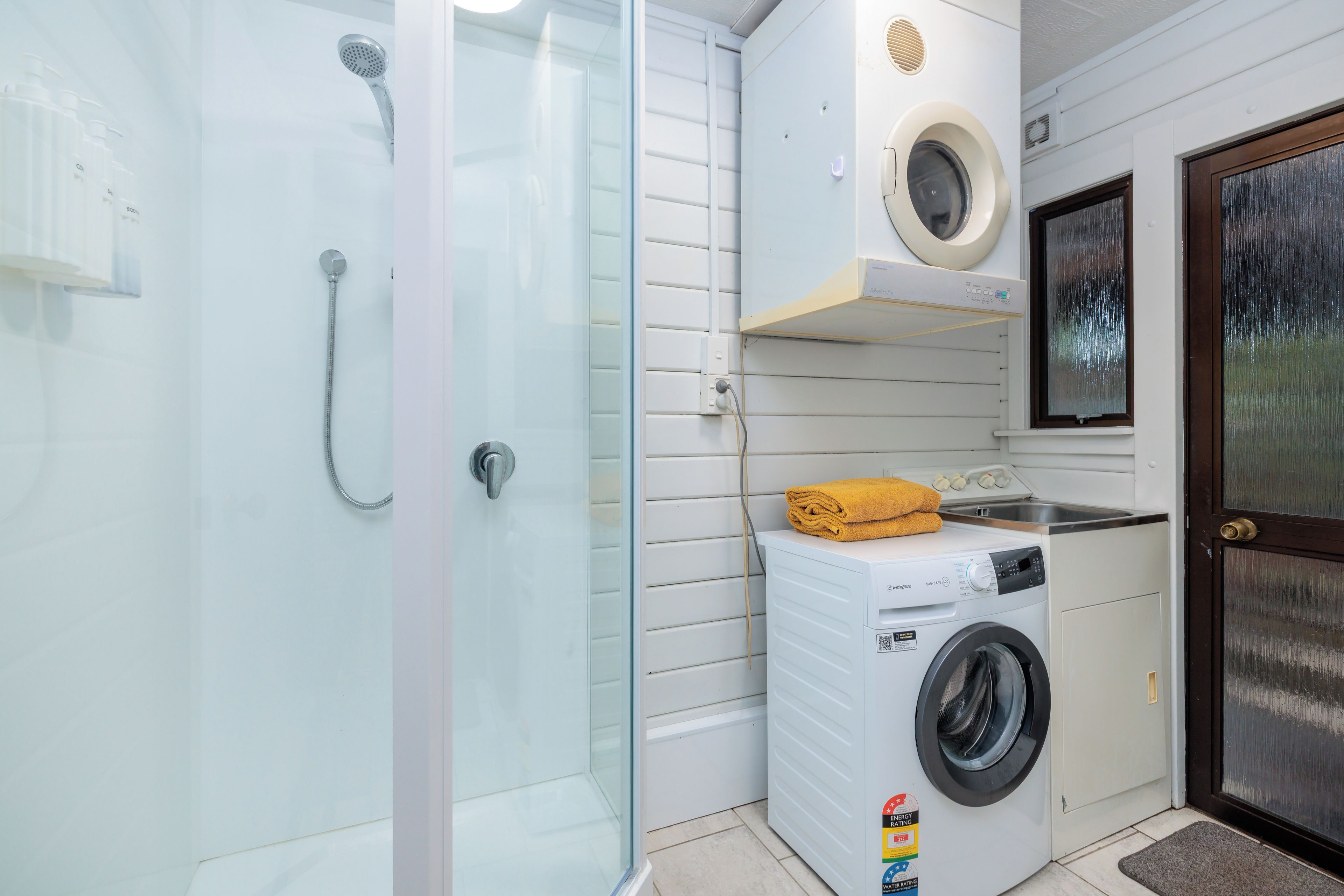 A compact bathroom with a glass shower enclosure, a washing machine, and a dryer.