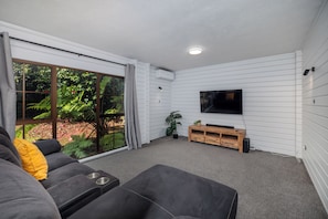 A living room with a sofa, a TV, and a sliding glass door leading to a garden.