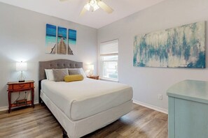 A bedroom with a bed, a nightstand, a window, and artwork on the walls. - Palm Bay 402 - Pool, Patio & Dog-Friendly (Corpus Christi)
