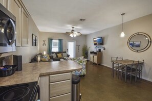 A compact kitchen with a central island, a dining area with a table and chairs, and a living space with a sofa and television. - Palm Bay 305 - Lagoon Pool, Patio & Dogs OK (Corpus Christi)