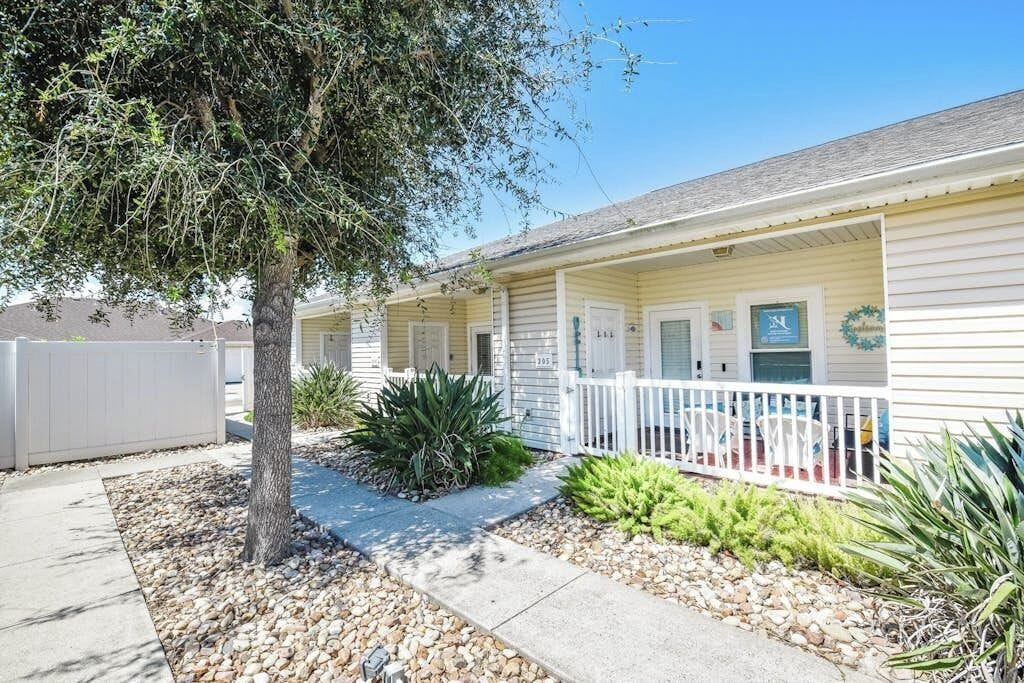 A single-story motel with a covered porch, a tree, and a small garden area with various plants.