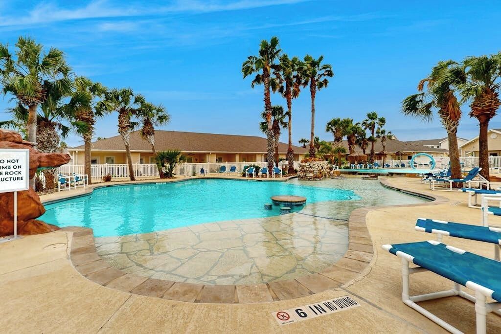 A pool area with lounge chairs, palm trees, and a sign indicating a no rock structure rule.