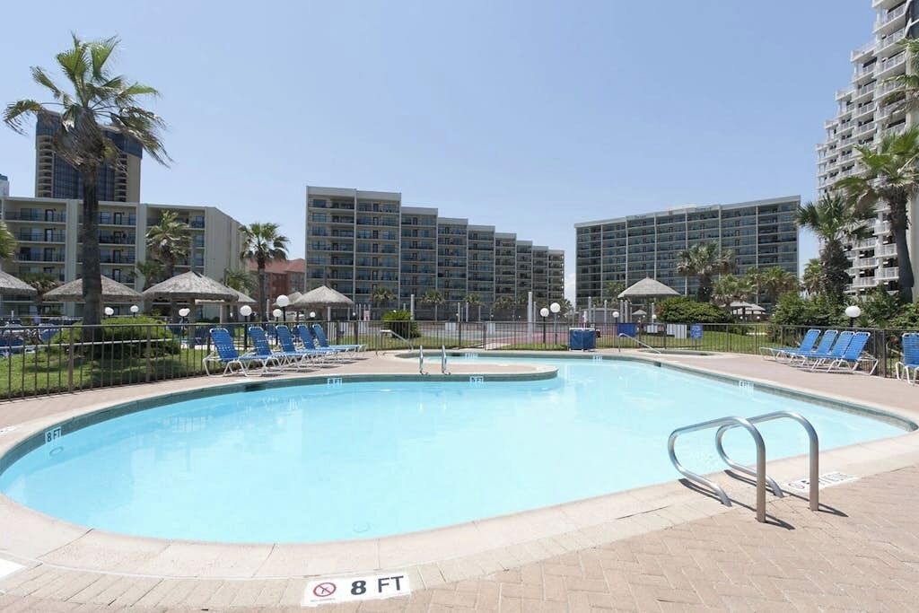 A swimming pool with lounge chairs and umbrellas, surrounded by high-rise buildings.