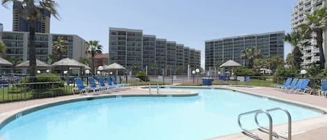 Una piscina con sillones de descanso y sombrillas, rodeada de edificios altos.