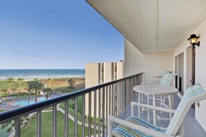 A balcony with a view of the beach, a pool, and a table with striped cushions. - Saida Towers IV #602 (South Padre Island)