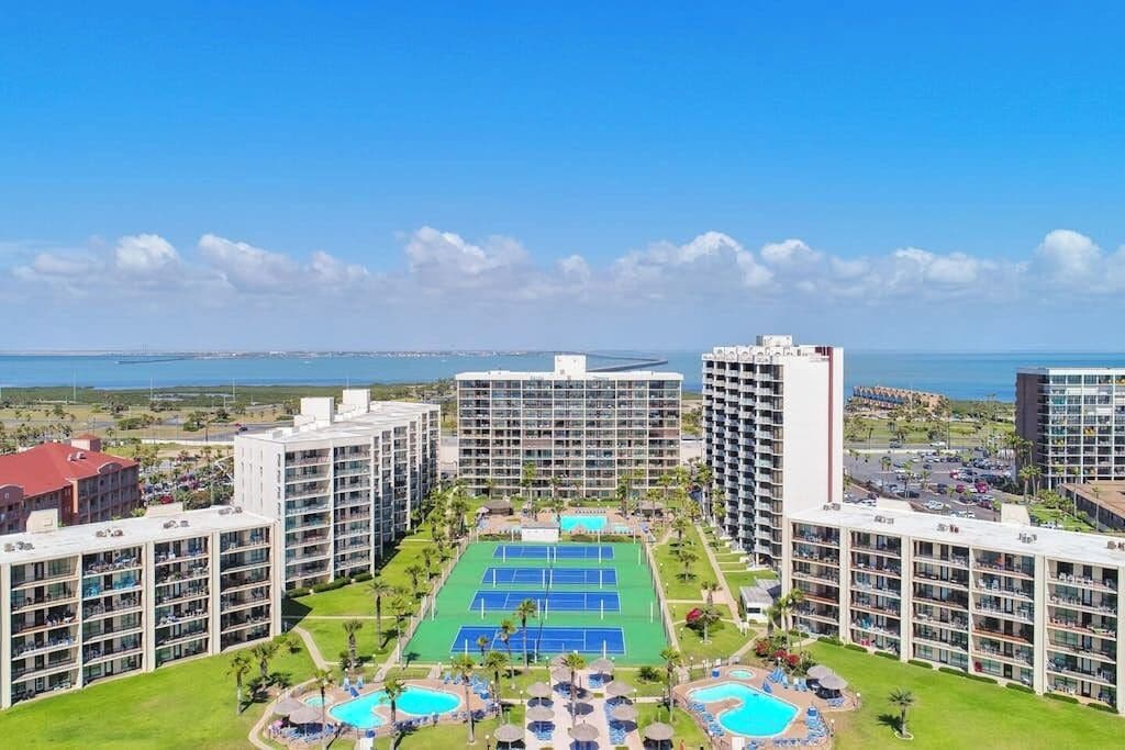 A hotel with multiple floors, a tennis court, and a pool area.