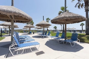 Un espace de détente aménagé sur la plage, avec des parasols en chaume et des chaises longues bleues.