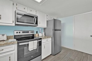 A kitchen with white cabinets, a stainless steel refrigerator, a microwave, an oven, and a toaster. - Saida Towers IV #602 (South Padre Island)