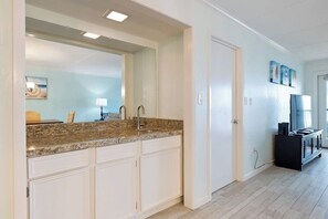 A modern kitchen with white cabinetry, granite countertops, and a large mirror above the sink. - Saida Towers IV #602 (South Padre Island)