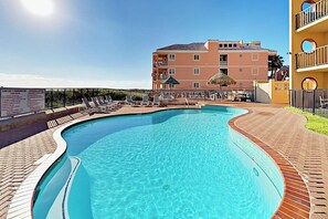 En swimmingpool med solstolar och en byggnad i bakgrunden.