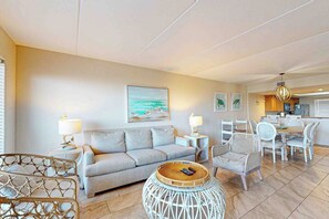 A modern living room with a sofa, chairs, a dining table, and a kitchen area in the background. - Suntide II Condominiums #101 (South Padre Island)