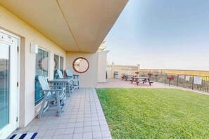 A balcony with a covered seating area, a grassy lawn, and a picnic table. - Suntide II Condominiums #101 (South Padre Island)