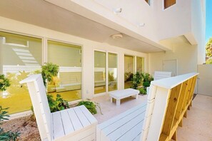 Eine moderne Außenpatio mit weißen Möbeln, einer Holzbank und einer Glastür zu einem überdachten Bereich.