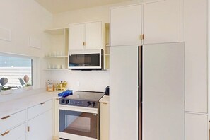 A modern kitchen with white cabinetry, a microwave, a stove, and a refrigerator. - Wabi Sabi Home - Pool & Bay Views, Steps to Sand (South Padre Island)