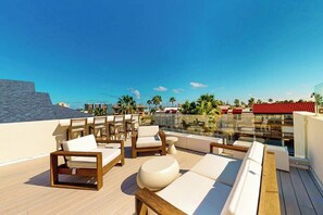 A rooftop terrace with outdoor seating, a glass balustrade, and a view of the cityscape. - Wabi Sabi Home - Pool & Bay Views, Steps to Sand (South Padre Island)