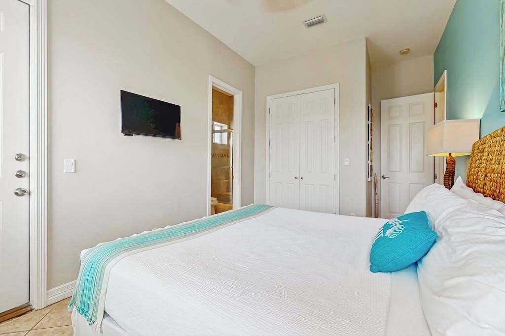Un dormitorio con cama, televisor montado en la pared y puerta que da a un baño.