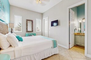 Une chambre à coucher avec un lit, une télévision et une salle de bain visible à travers une porte ouverte.