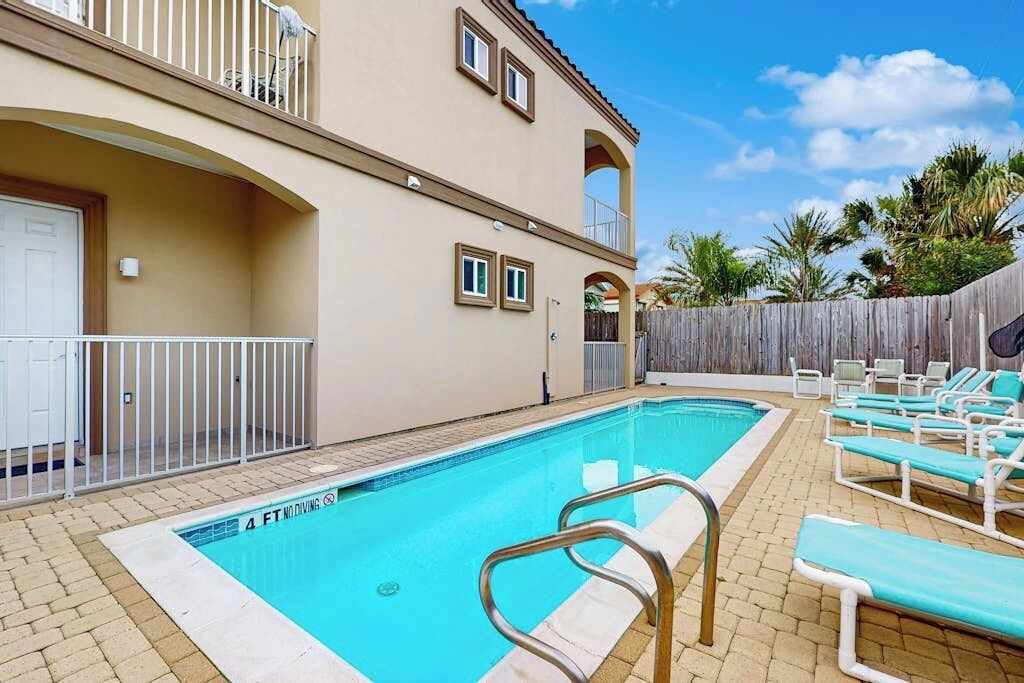 A swimming pool with a safety sign, lounge chairs, and a building with balconies.