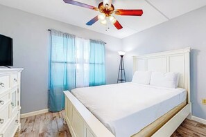 Een slaapkamer met een bed, een plafondventilator, een lamp en een raam met gordijnen.