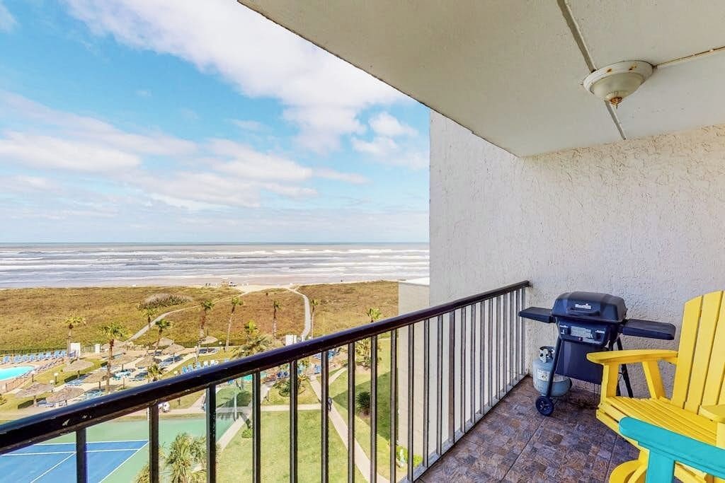 A balcony with a view of the beach and a grill.