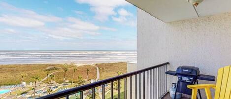 A balcony with a view of the beach and a grill.