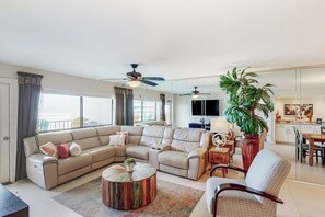 Ein geräumiges Wohnzimmer mit einem Ecksofa, einem Couchtisch und einer großen Kübelpflanze.