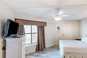 Ein Hotelzimmer mit einem Bett, einem Fernseher auf einem Schrank, einem Deckenventilator, einem Fenster mit Vorhängen und einer Tür.