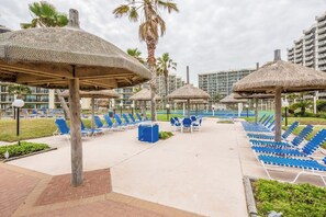 A resort pool area with thatched umbrellas, blue lounge chairs, and a clear view of the pool. - Saida Towers IV #4802 (South Padre Island)