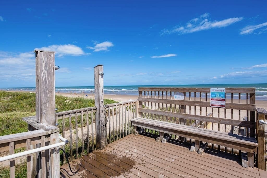 A wooden boardwalk leading to a beach with a clear blue sky.