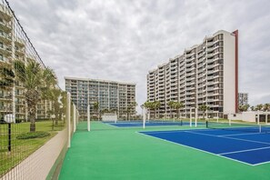 Un court de tennis avec un filet, entouré d’une clôture, et situé à côté d’immeubles de grande hauteur.
