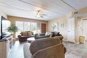 A living room with a ceiling fan, a television, a sofa set, a coffee table, and a potted plant. - Beachview Condominiums #111 (South Padre Island)