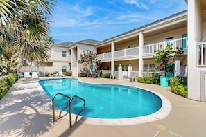 A swimming pool with a curved edge, surrounded by a covered patio area with white railings and lounge chairs. - Las Puertas Condominiums 201 (South Padre Island)